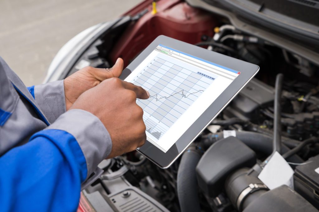 man using a tablet next to an open car engine